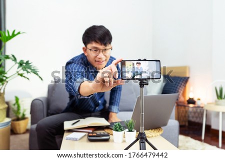 Young asian male blogger recording vlog video on camera review of product at home office, Focus on tripod mounted camera screen broadcast live stream video to a social network