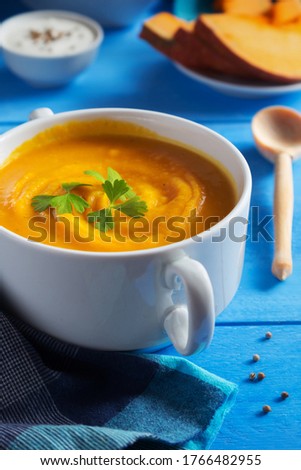 Vertical photo of pumpkin cream soup with seeds and croutons on blue background