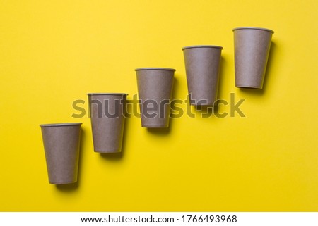 Five eco-friendly cardboard cups lie on diagonal on a yellow color paper background. Mock-up. Close-up.