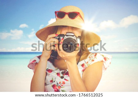 Caucasian woman taking photo with dslr camera on the beach while wearing hat during summer day