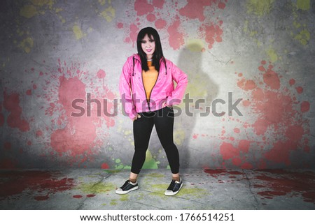 Pretty female hip-hop dancer smiling at the camera while standing against painted wall