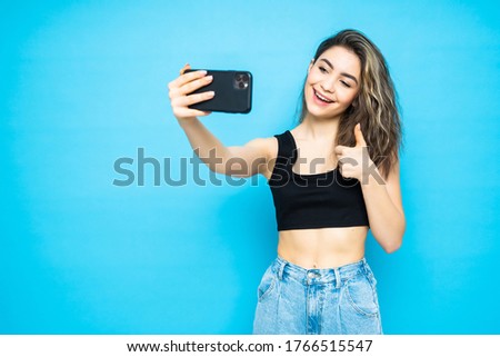 Portrait of a young attractive woman making selfie photo with smartphone isolated on a blue background