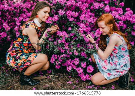 Picture of a cute girl in a summer dress enjoys plants in the botanical garden with her older sister..