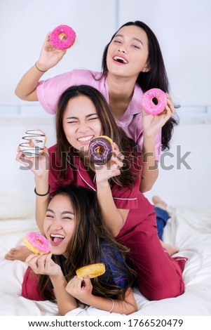 Group of cheerful teenage girls holding donuts while playing together on the bed at home