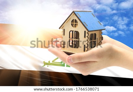 The concept of real estate mortgages, citizenship and accommodation, as well as investment in a future home. In hands holding a model of a wooden house against the background of the flag of Iraq.