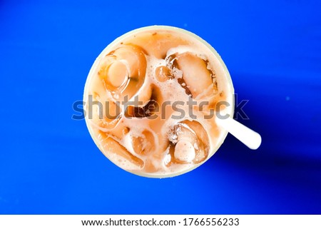 Flatlay and selective focus picture of "teh ais" or milk icea tea serve in Malaysia breakfast on blue table.