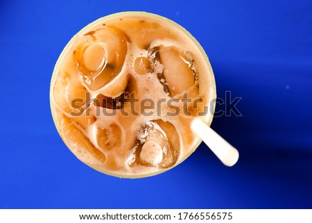 Flatlay and selective focus picture of "teh ais" or milk icea tea serve in Malaysia breakfast on blue table.