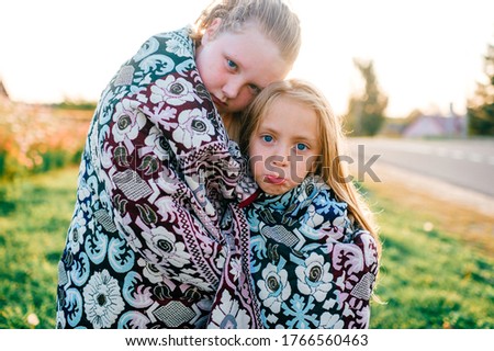 Picture of beautiful caucasian girl with her older sister froze, wrapped up in a veil and stand outdoors, morning in a village in summer