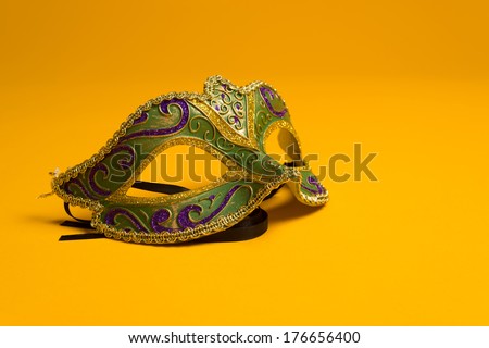 Green, gold, purple mardi gras mask on a bright yellow background