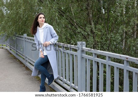 
Portrait of a beautiful young woman in a white hoodie and blue jeans with dark hair developing in the wind and brown eyes in a city landscape