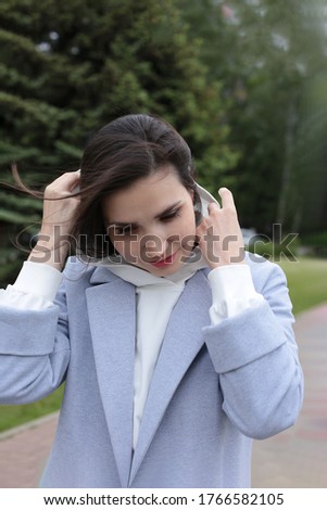 
Portrait of a beautiful young woman in a white hoodie and blue jeans with dark hair developing in the wind and brown eyes in a city landscape