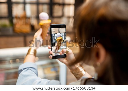 Young woman making a photo of yummy ice cream in waffle cone indoors. Buying ice cream at the shop