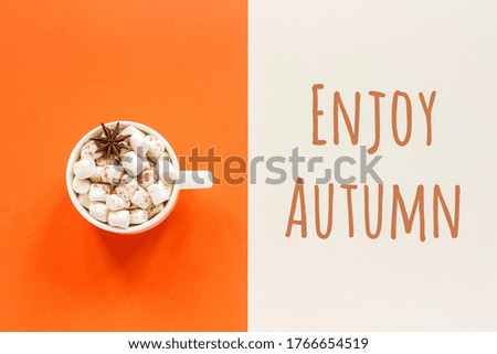 Enjoy Autumn text and cup of cocoa with marshmallows on orange beige background. Concept fall mood. Top view Flat lay Postcard.