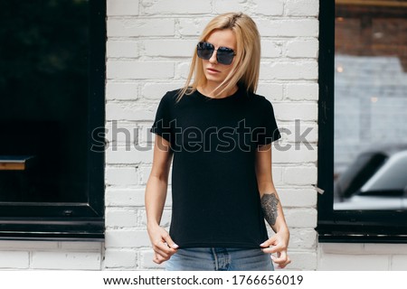 Stylish blonde girl wearing black t-shirt and glasses posing against street , urban clothing style. Street photography Royalty-Free Stock Photo #1766656019