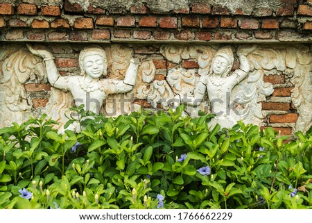 The image of Buddhist saints on the temple wall is overgrown with plants.