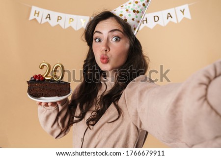Image of surprised woman taking selfie photo with birthday cake isolated over beige background
