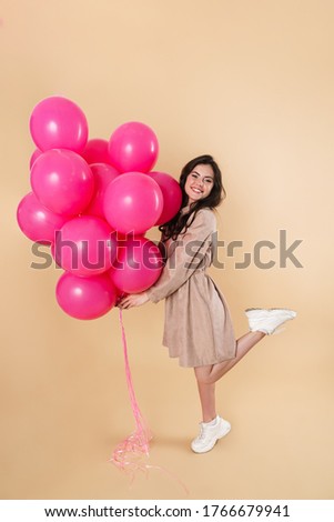 Image of excited cute woman smiling while posing with pink balloons isolated over beige background
