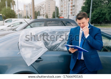 A man writes in a tablet next to the car. An accident on the road, the airbag didn't work. Accident, causing damage to a young man. Insur the car after the accident