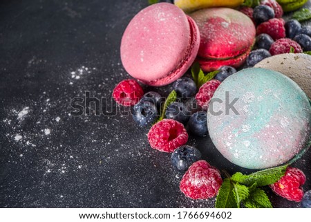 Colorful french macaron dessert. Set of various different tastes and color macaron cookies with berries, sugar powder and mint on dark grey stone background