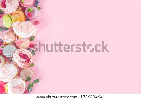 Colorful french macaron dessert. Set of various different tastes and color macaron cookies with berries, flowers, sugar powder and mint on pink background