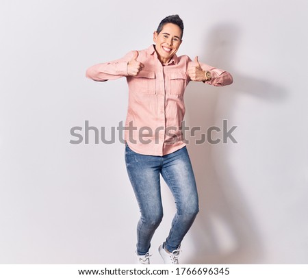 Young beautiful caucaisan woman with short hair wearing casual clothes smiling happy. Jumping with smile on face doing ok sign with thumbs up over isolated white background