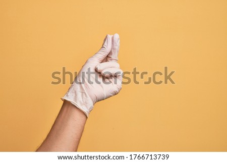Hand of caucasian young man with medical glove over isolated yellow background holding blank space with thumb finger, business and advertising