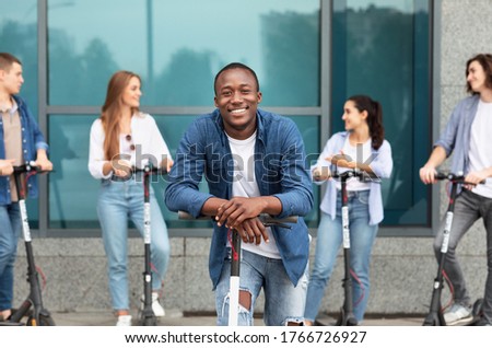 Youth Concept. African american guy leaning on e-scooter, looking at camera, spending time with friends
