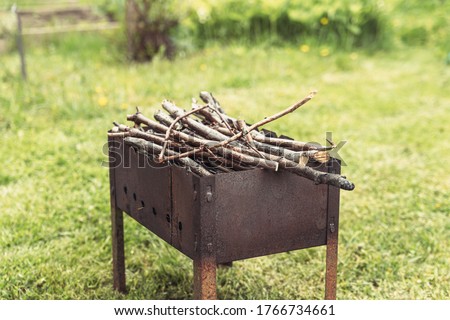 An old rusty barbecue filled with dry twigs for lighting a fire on a background of green grass