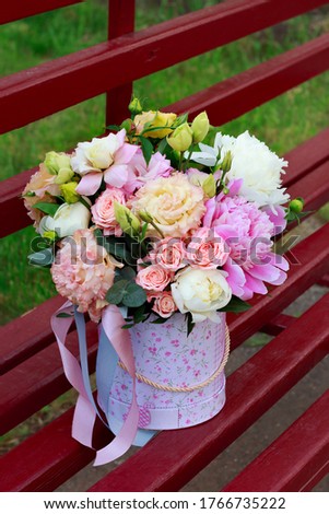 beautiful hatbox with flowers on a bright red bench, close-up with a blurry background. peony, eustoma, Bush rose, eucalyptus, ribbons