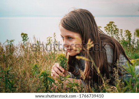 Little girl child with long hair lying on the grass and touching flowers, copy space