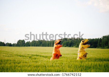 Two yellow and orange dinosaur dino tyrannosaurus running biting each other and having fun in green field. Shot from air. aerial shot. Dinosaur playing small guitar