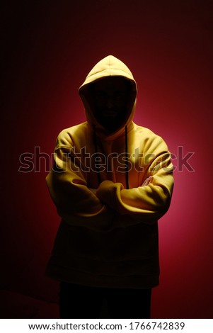An unknown man without a face in a yellow sweatshirt is standing against a red wall. The concept of modern fashion photography.