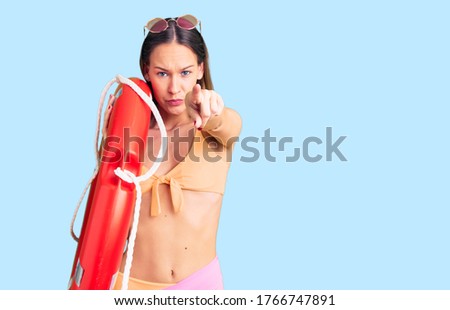 Beautiful brunette young woman wearing bikini and holding lifesaver float pointing with finger to the camera and to you, confident gesture looking serious 