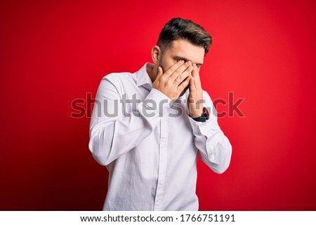 Young business man with blue eyes wearing elegant shirt standing over red isolated background rubbing eyes for fatigue and headache, sleepy and tired expression. Vision problem