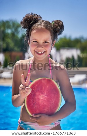a girl in a swimsuit stands with a watermelon on the beach.