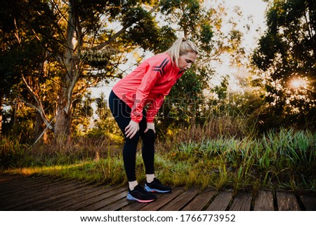 Athletic woman tired from run in the park, bent over breathing heavily