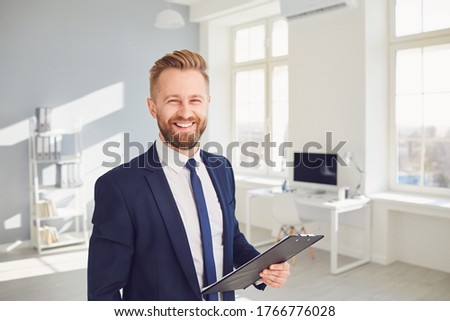 Positive businessman worker manager holds a clipboard in his hand smiling works in modern office.