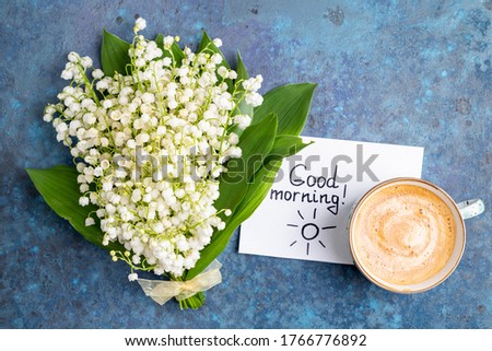 Notes good morning and coffee mug with bouquet of flowers lily of the valley on blue background. Breakfast, morning coffee, card concept, top view