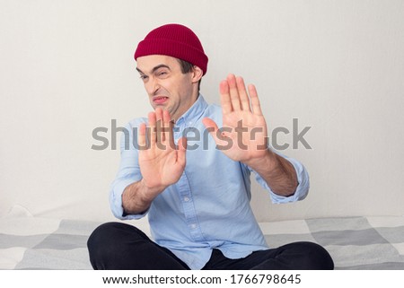 Frightened man shows a stop sign with his hands, man at home on self-isolation, portrait 