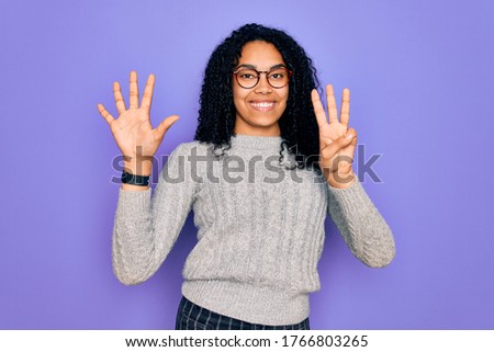 Young african american woman wearing casual sweater and glasses over purple background showing and pointing up with fingers number eight while smiling confident and happy.