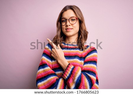 Young beautiful blonde girl wearing glasses and casual sweater over pink isolated background cheerful with a smile on face pointing with hand and finger up to the side, happy and natural expression