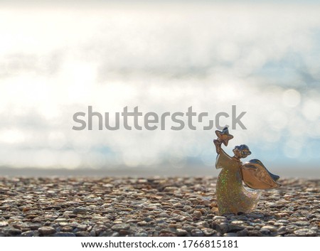 Angel shape on gravel floor in bokeh of sea .Angel and miracle. Faith in God. Pray for you. Miracle from heaven. Believe in goddess. Christianity background concept.