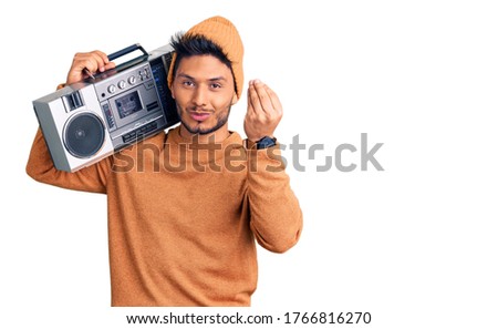 Handsome latin american young man holding boombox, listening to music doing italian gesture with hand and fingers confident expression 