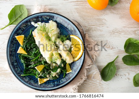 flat lay of a plate with fried halibut fillet with orange sauce and spinach garnish on a light table