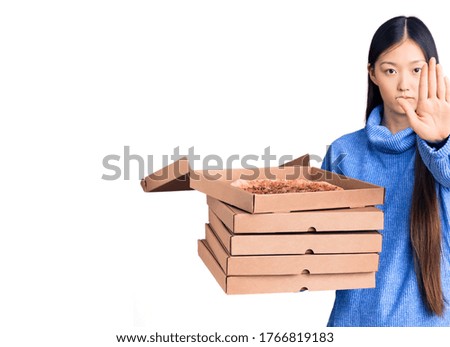 Young beautiful chinese woman holding cardboard boxes of italian pizza with open hand doing stop sign with serious and confident expression, defense gesture 