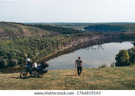 A biker dressed in motorcycle equipment on distance. Motorcycle for long journeys, extreme lifestyle, tourism and vacation, dark colors. Canyon with the river. Copy space. Dniester Ukraine
