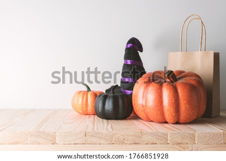 Holiday concept with Halloween pumpkin decor and gift paper bag on wooden table. Creative Halloween minimal concept.