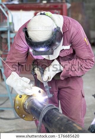 Craftsman in a safety suit is welding a metal pipe Royalty-Free Stock Photo #176685620