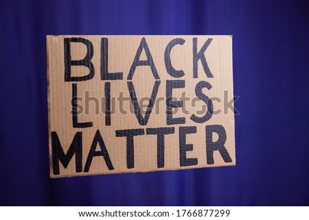 BLACK LIVES MATTER on a blue blurred background. No racism concept. Cardboard banner with a text "Black Lives Matter". Concept of the struggle for equality
