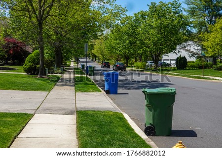 View of a residential tree lined street with green and blue trash bins lined up along the curb for trash truck collection. Royalty-Free Stock Photo #1766882012
